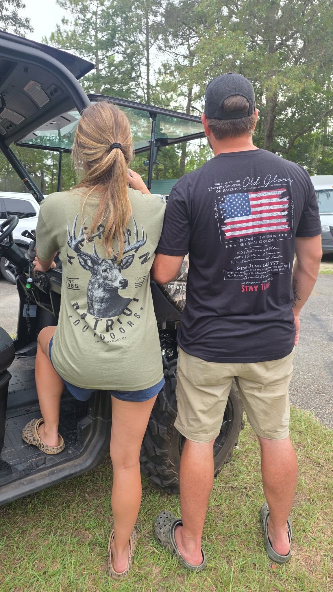 Couple wearing TAP Whitetail Deer and Old Glory graphic tees beside a UTV