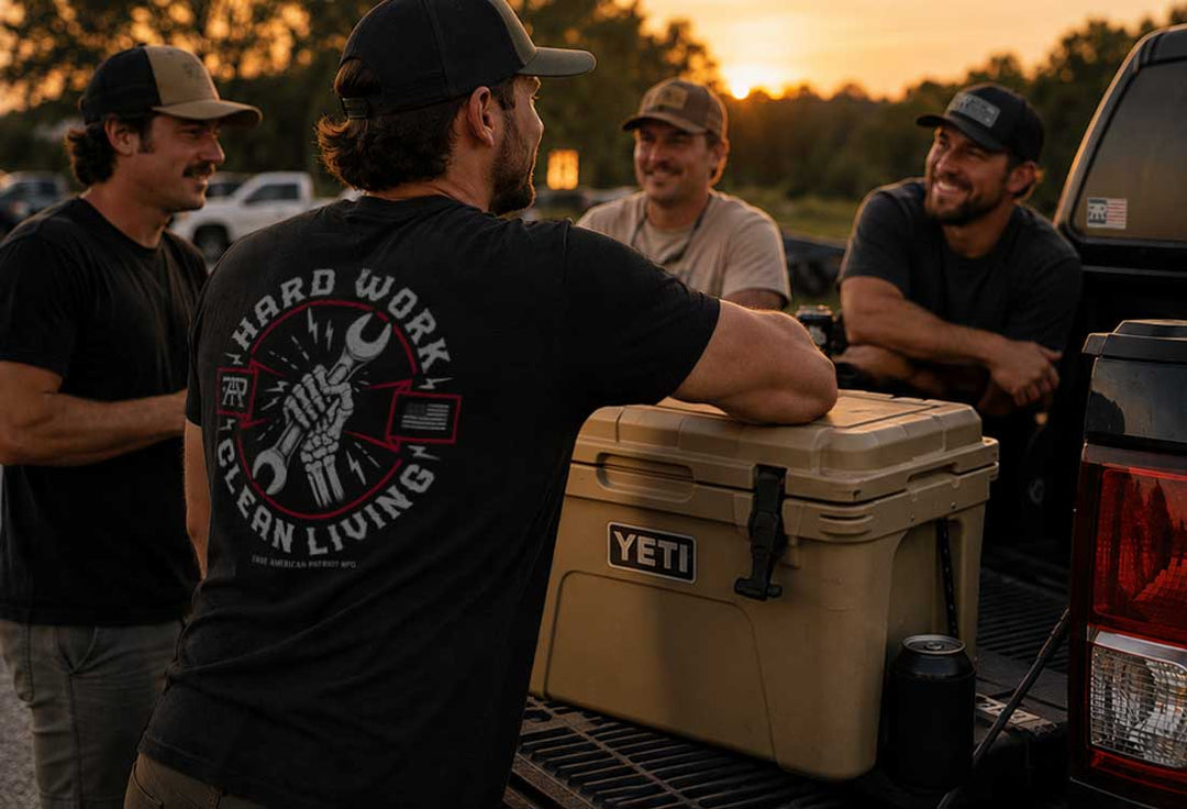 Group of friends wearing True American Patriot apparel gathered around a truck tailgate and cooler at sunset, representing blue-collar lifestyle and American values.