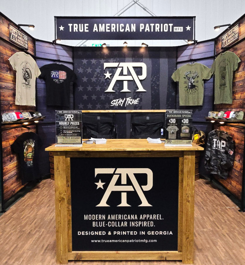 True American Patriot MFG booth displaying graphic tees and hats at Georgia Buckarama
