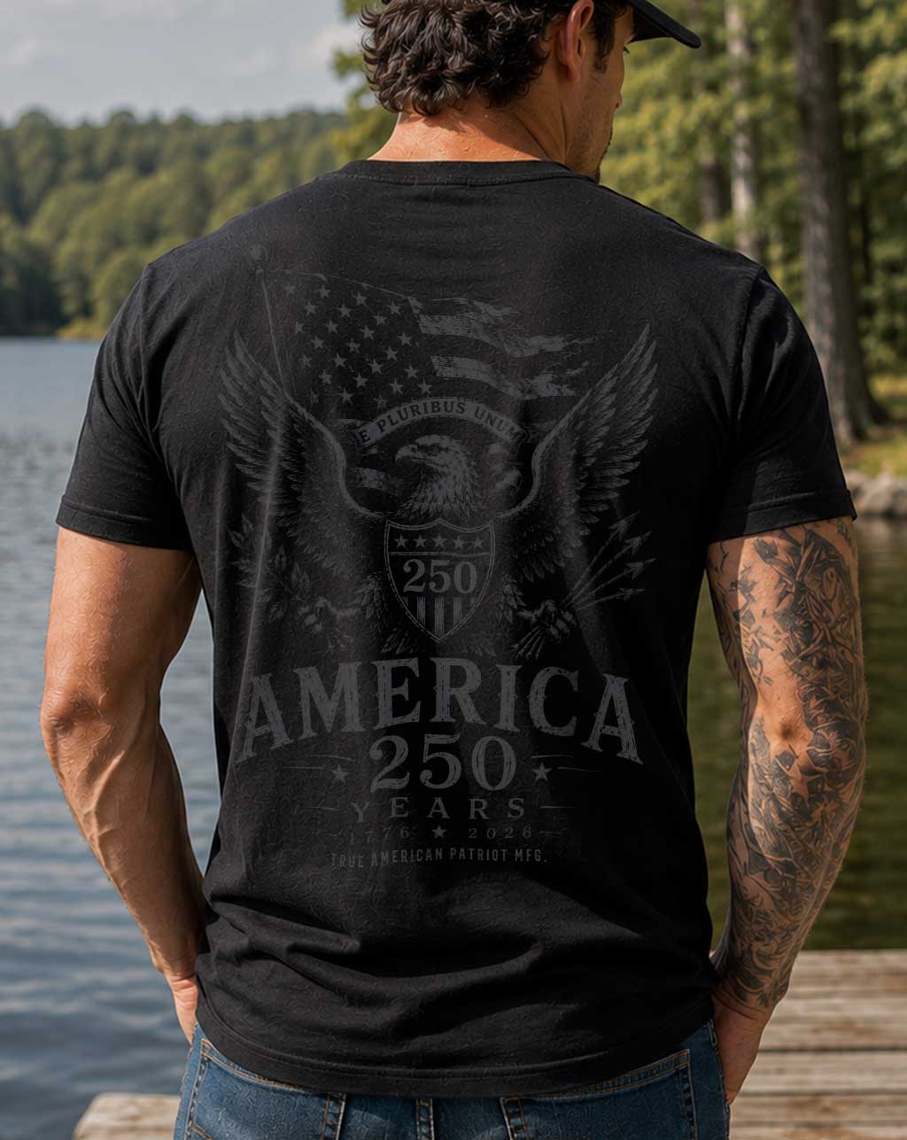 Man wearing a black True American Patriot Mfg America 250 Years E Pluribus Unum Eagle T-Shirt standing on a dock on a lake
