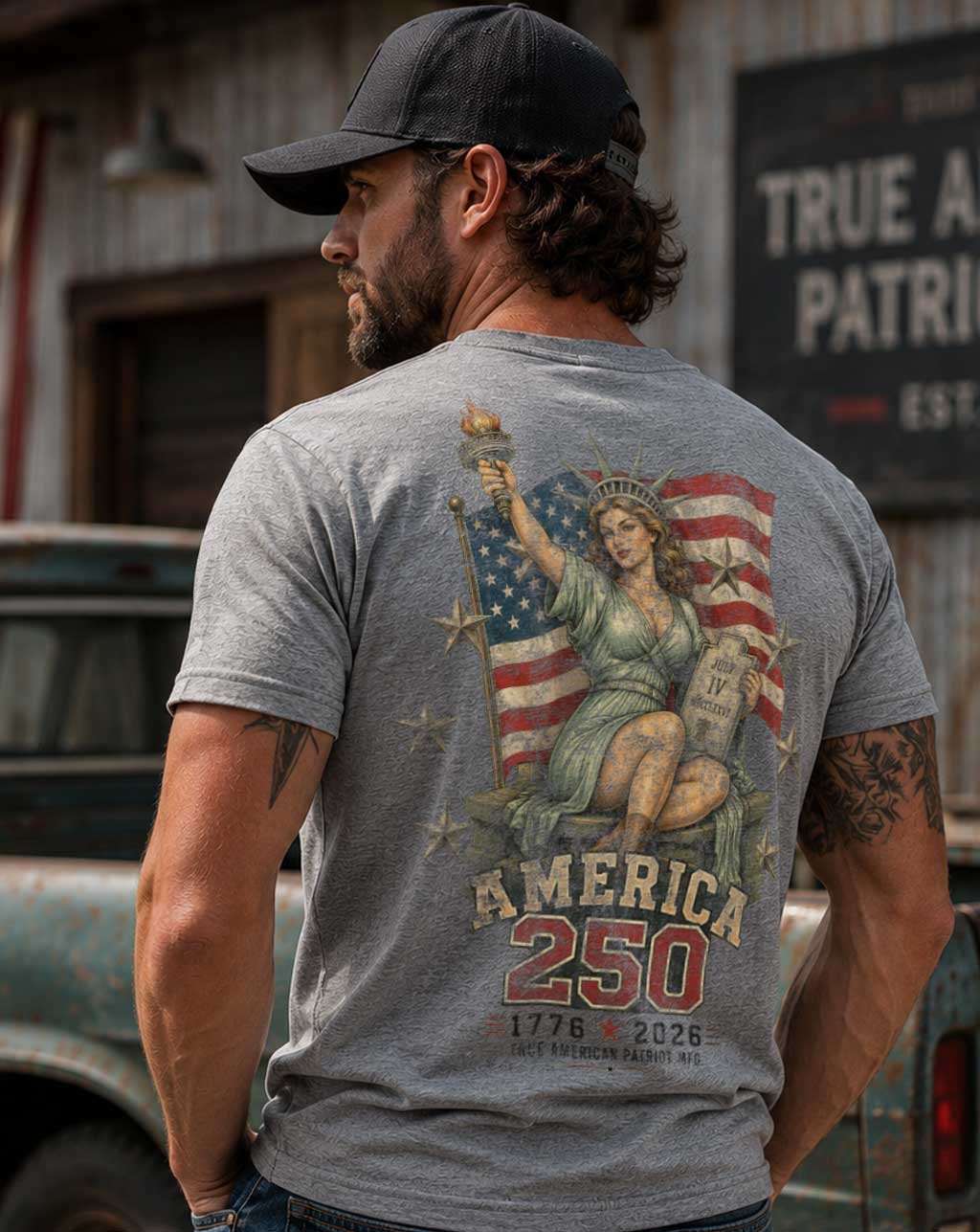 Man wearing a dark heather gray True American Patirot Mfg American 250 Lady Liberty t-shirt, standing in front of a rustic background.