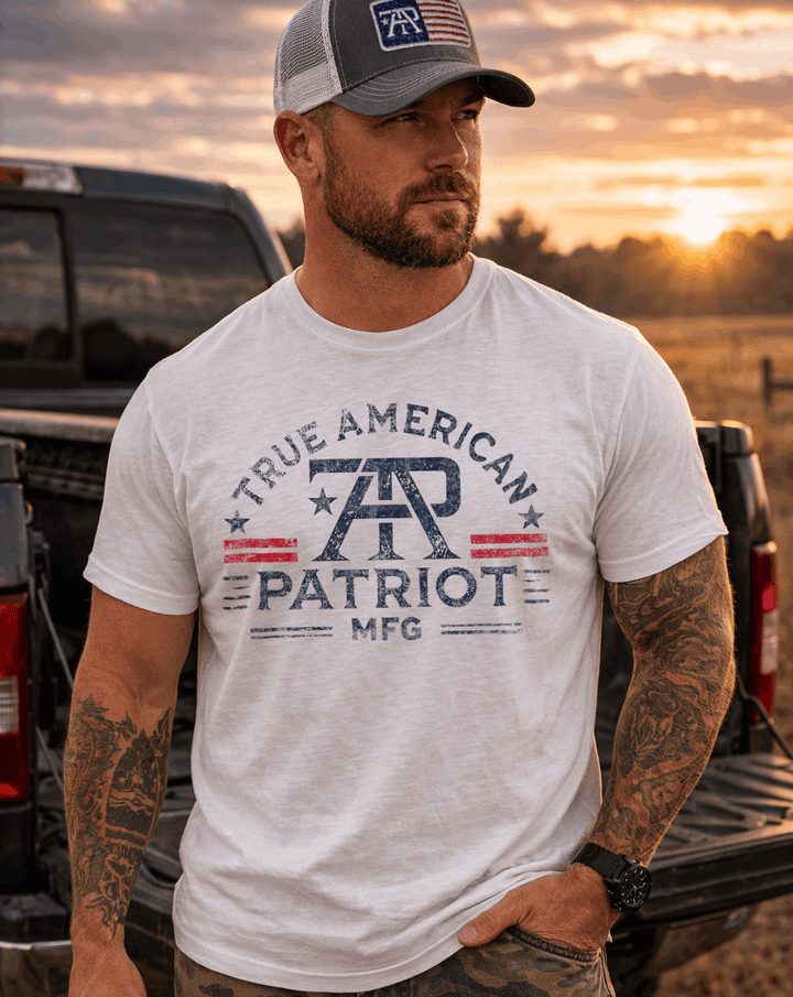 Man wearing a True American Patriot Mfg - Branded Tee and Flag Patch Hat standing in front of his truck with the sun setting in the background