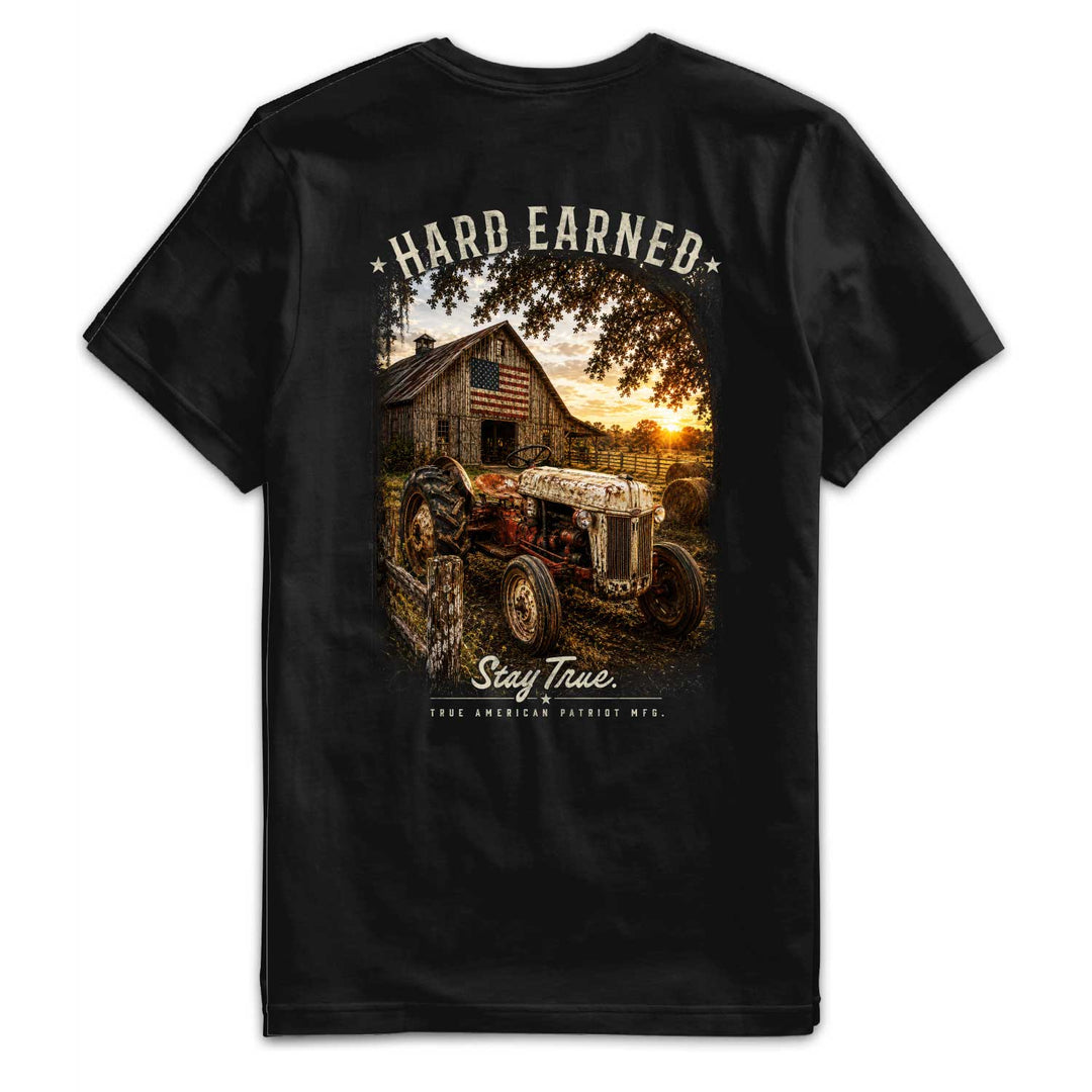 Back of the Hard Earned Heritage Tee featuring a vintage tractor, weathered American barn, and sunset farm scene with "Hard Earned" artwork by True American Patriot MFG.