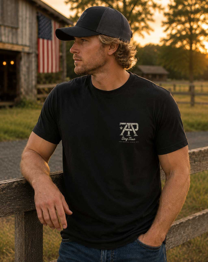 Man wearing a Heritage Collection Tee by True American Patriot MFG featuring the TAP Stay True left chest logo, photographed at sunset in front of a rustic American barn in rural Georgia.