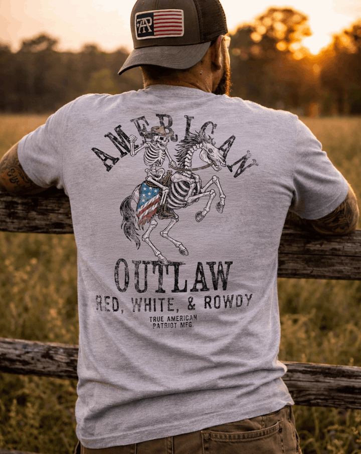 Man wearing True American Patriot Mfg Flag Patch Hat and American Outlaw - Red, White, &amp; Rowdy Tee leaning on Fencepost watching the sunset
