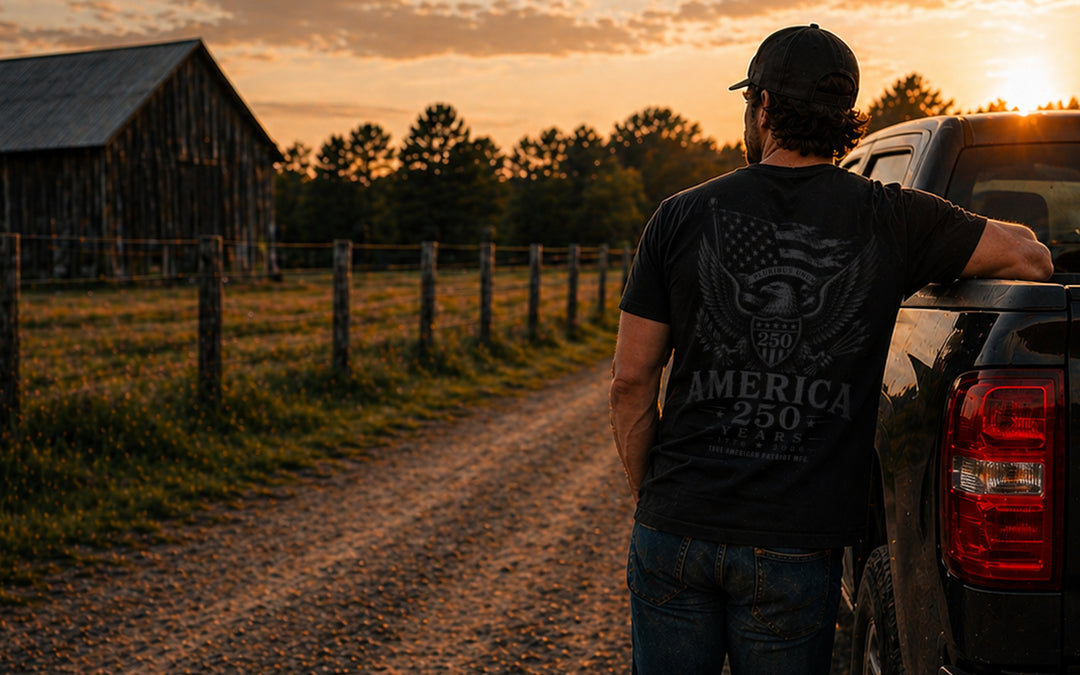 America 250 patriotic graphic tee by True American Patriot MFG worn beside a pickup truck on a rural American backroad at sunset